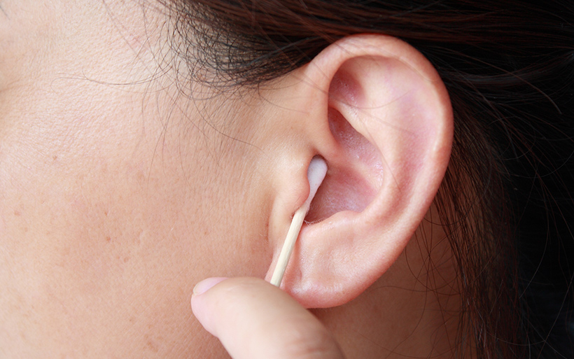 A person gently cleaning the inside of their ear with a cotton swab.
