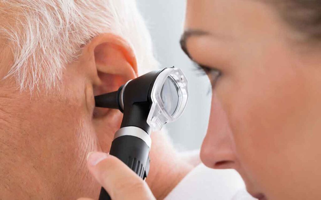 A healthcare professional uses an otoscope to examine the ear of an older adult with gray hair during a medical check-up.
